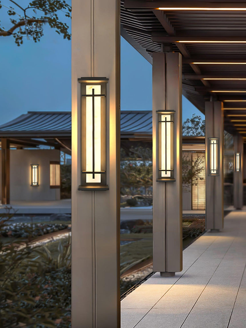 Lanterns lit along a colonnade walk beside clipped shrubs at dusk