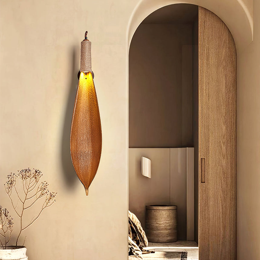 The leaf sconce lit on a plaster wall beside an arched wood doorway