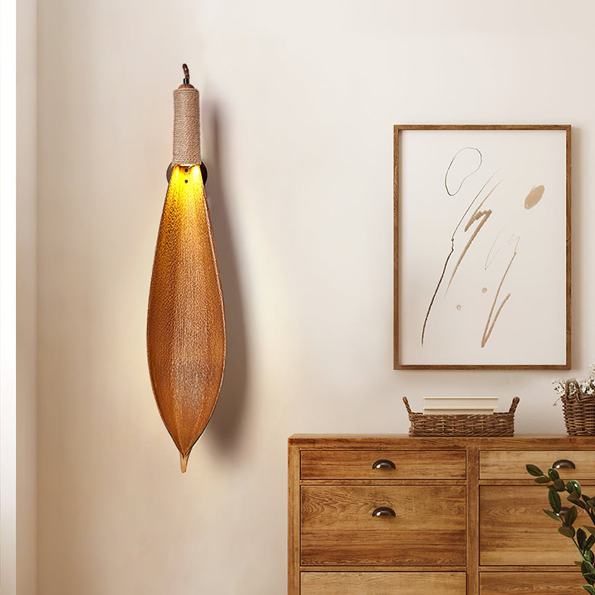 The leaf sconce lit above a wood chest of drawers beside a framed line drawing
