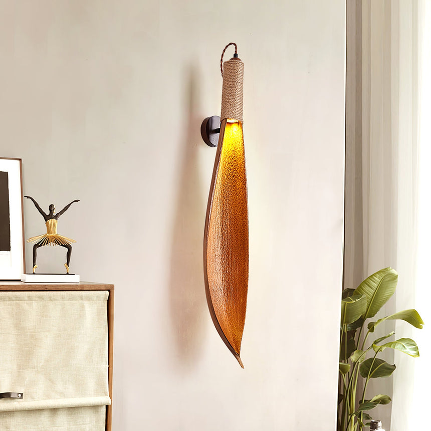 The leaf sconce lit between a sideboard with a figure and a large plant