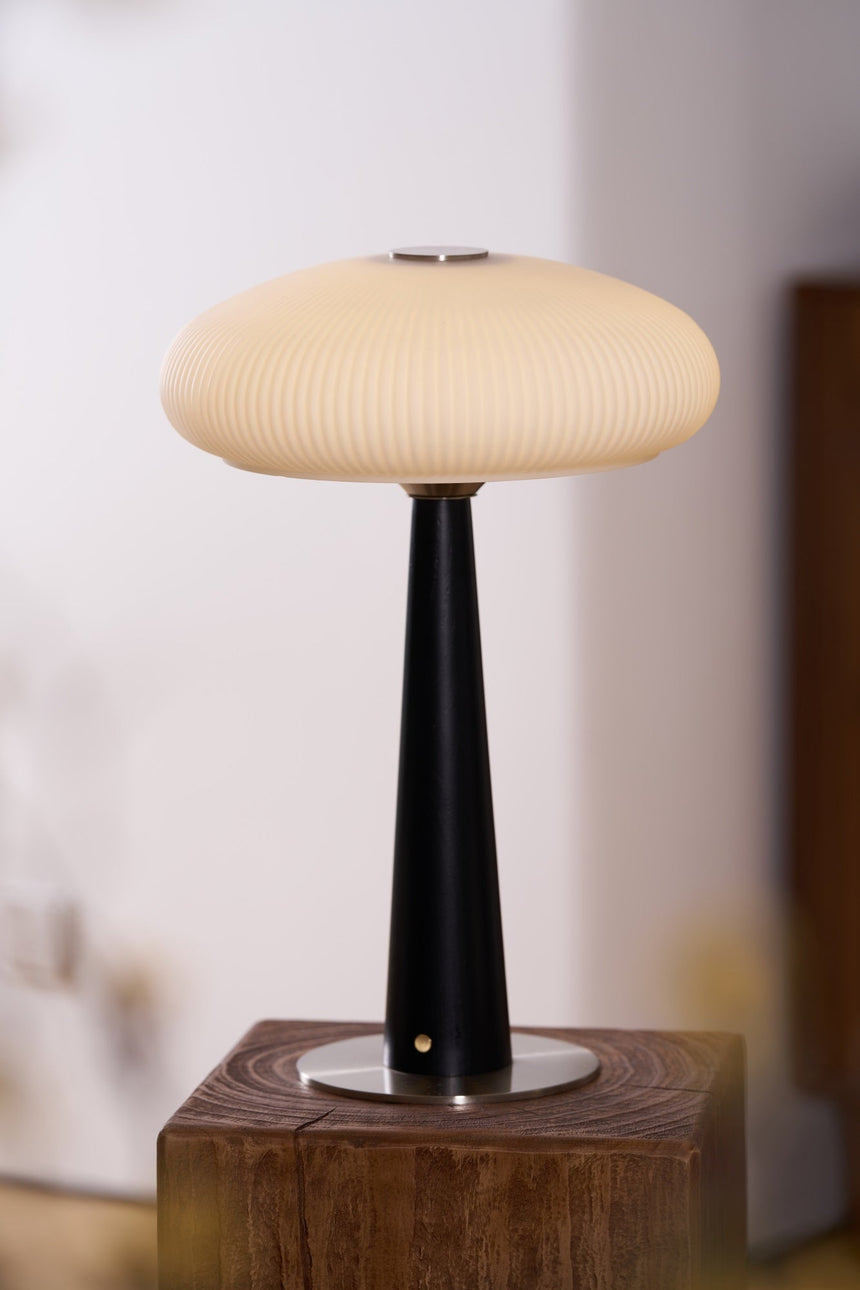 LED table lamp lit on a plinth beside a small vase of blossom