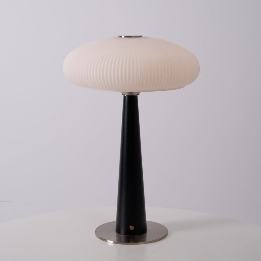 LED table lamp lit in a warm tone on a wooden plinth in a pale room