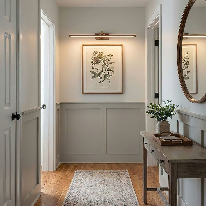 Walnut tone bar lit above a framed print in a hallway with a console and a mirror