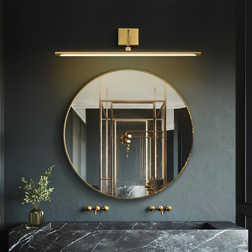 Brass bar lit above a round mirror on a dark wall over a marble basin and plants