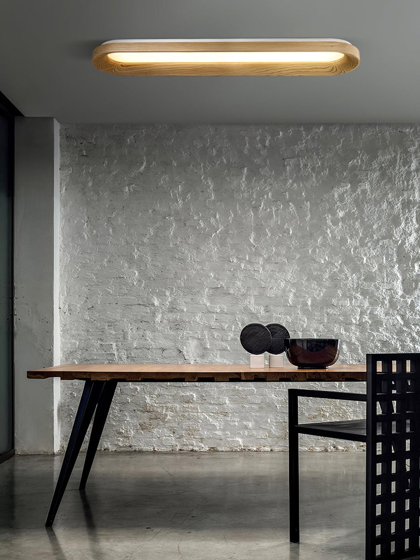 Linear wood frame ceiling light above a dark dining table with a textured wall