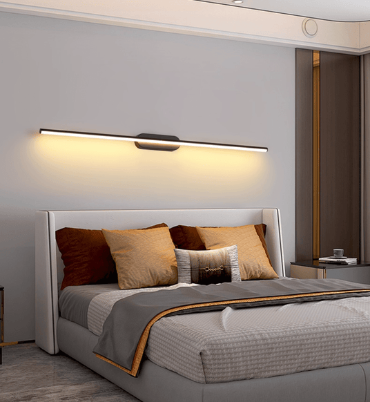 Thin rod lit above a wide bed with a gold trimmed headboard in a gray bedroom