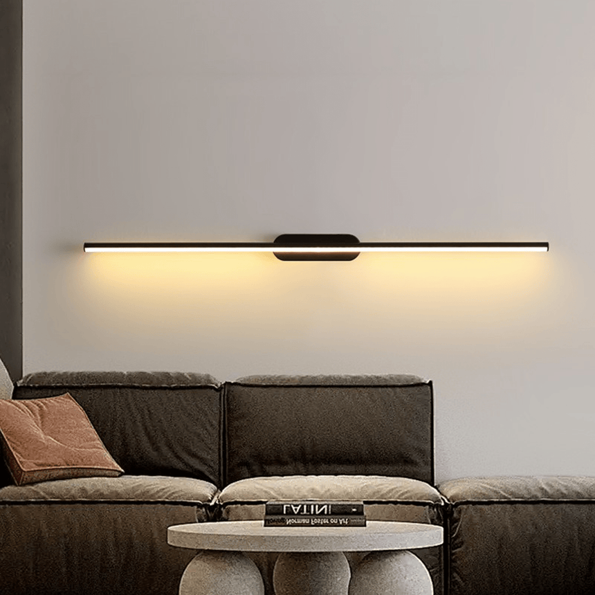 Thin rod lit on a wall above a low sofa with cushions and a round table