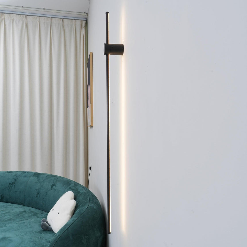 Lit beside a long curtain above a green armchair in a pale corner of a room