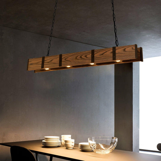 Lit above a dining table with stacked plates and a glass bowl against a dark wall