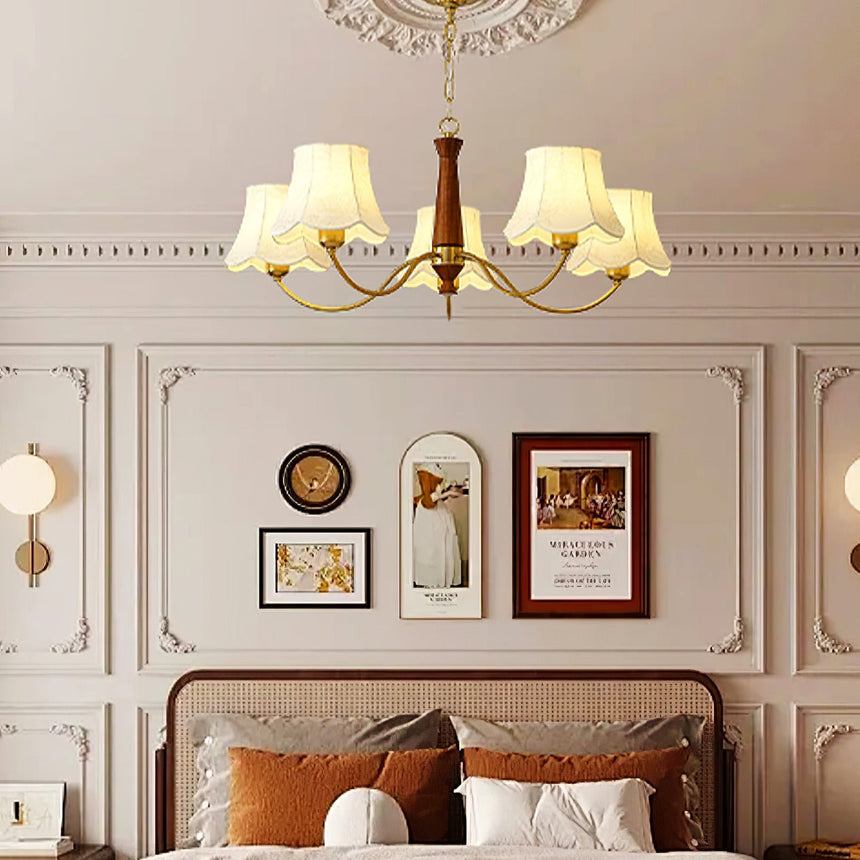 Chandelier lit in a bedroom above a bed with rust colored pillows