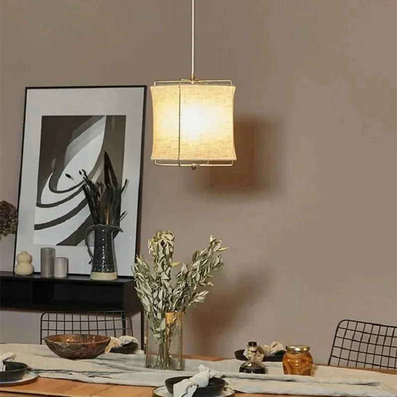 Linen drum pendant light over a dining table beside framed artwork