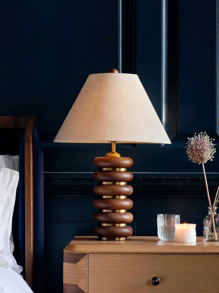 Linen shade table lamp lit on a nightstand against a dark wall