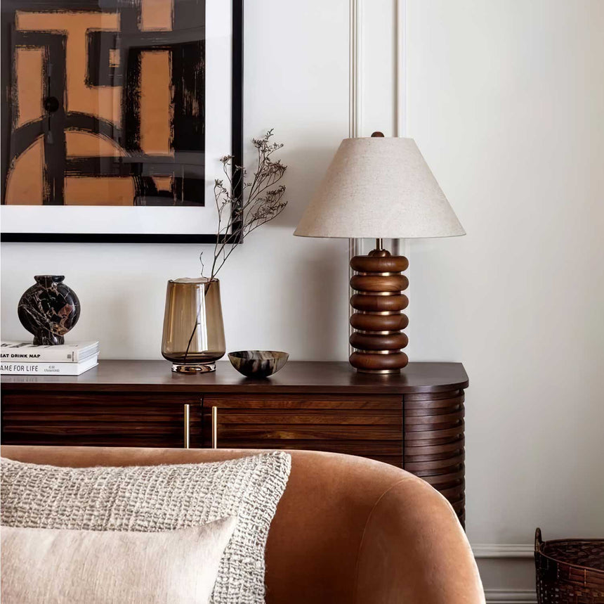Linen shade table lamp on a dark sideboard beside a vase