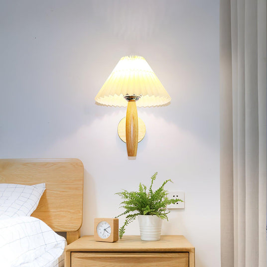 Sconce lit above a wood nightstand with a small plant beside a bed