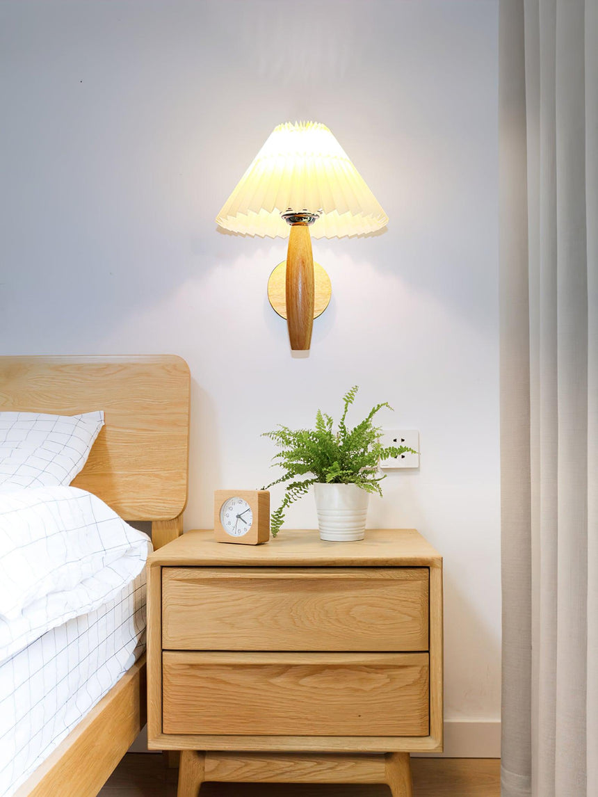 Sconce lit above an oak nightstand holding a plant and a small clock