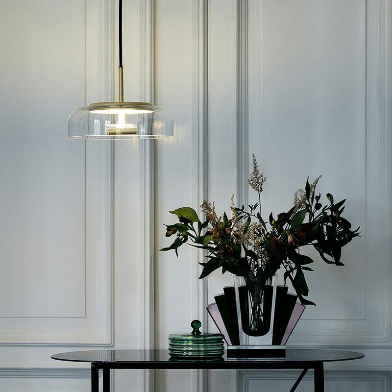 A clear glass dome pendant lit above a table with a plant and stacked books