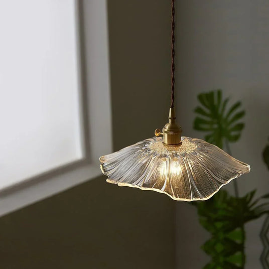 A clear lotus shade lit beside a trailing plant and a framed print