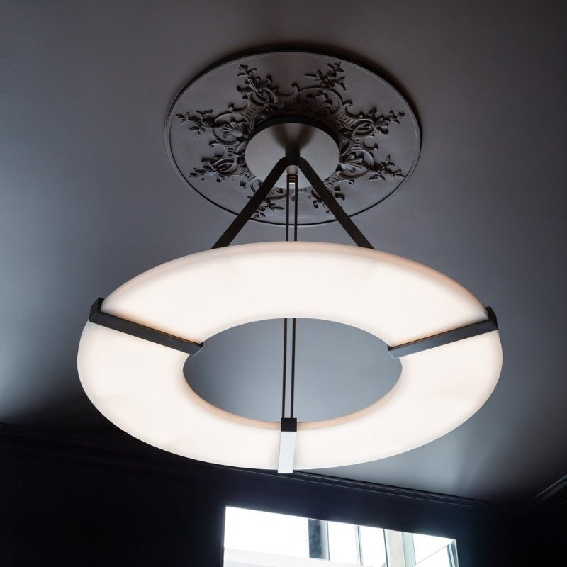 The lit ring below a plaster ceiling rose in a room with a tall window