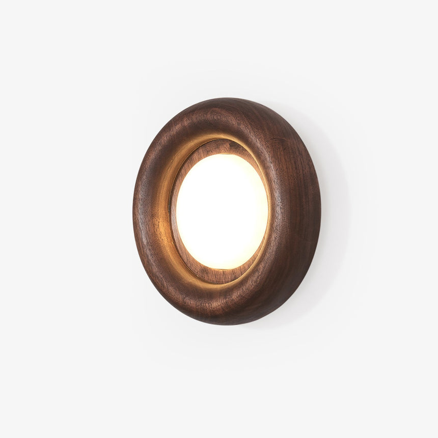 Low profile wall sconce, a rounded wood ring with a lit disc at its center