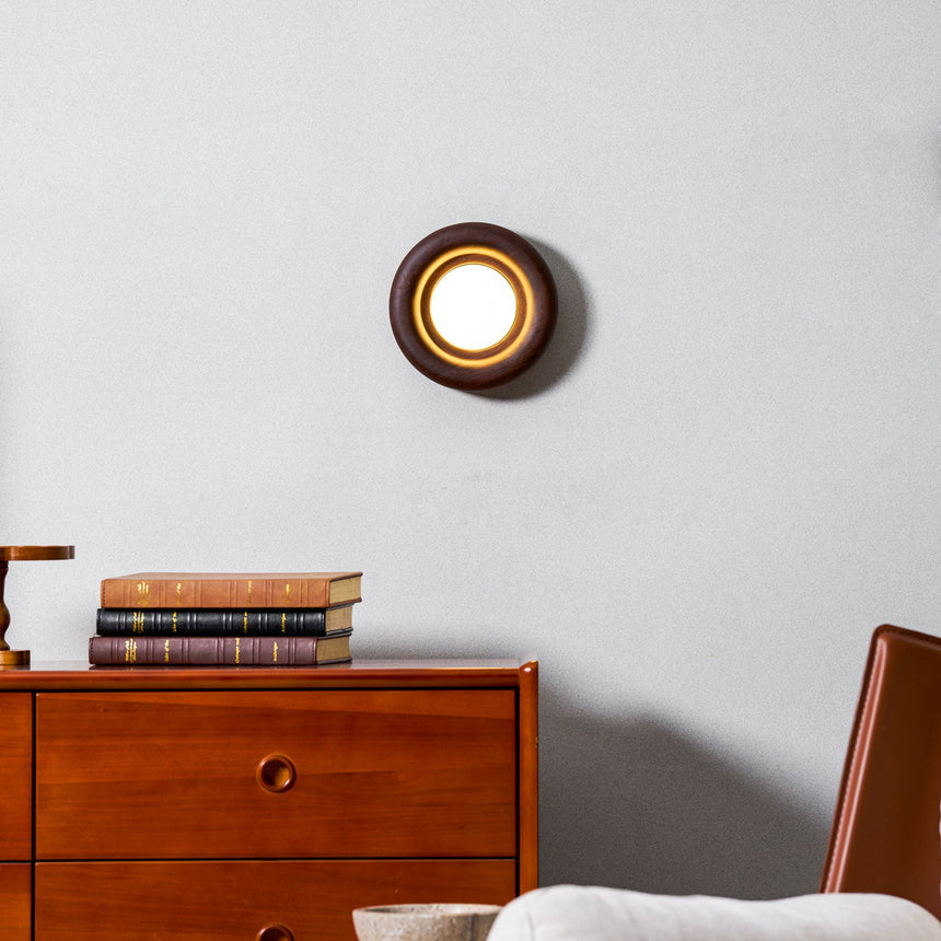Sconce lit on a wall above a teak dresser stacked with old hardback books