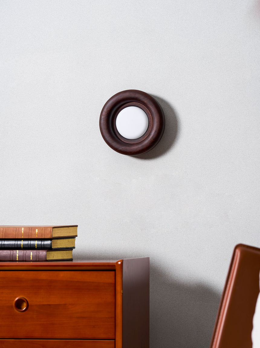 Sconce unlit above a teak dresser with books, an armchair to one side