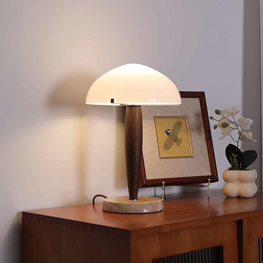 Marble base table lamp lit on a wood sideboard beside framed art