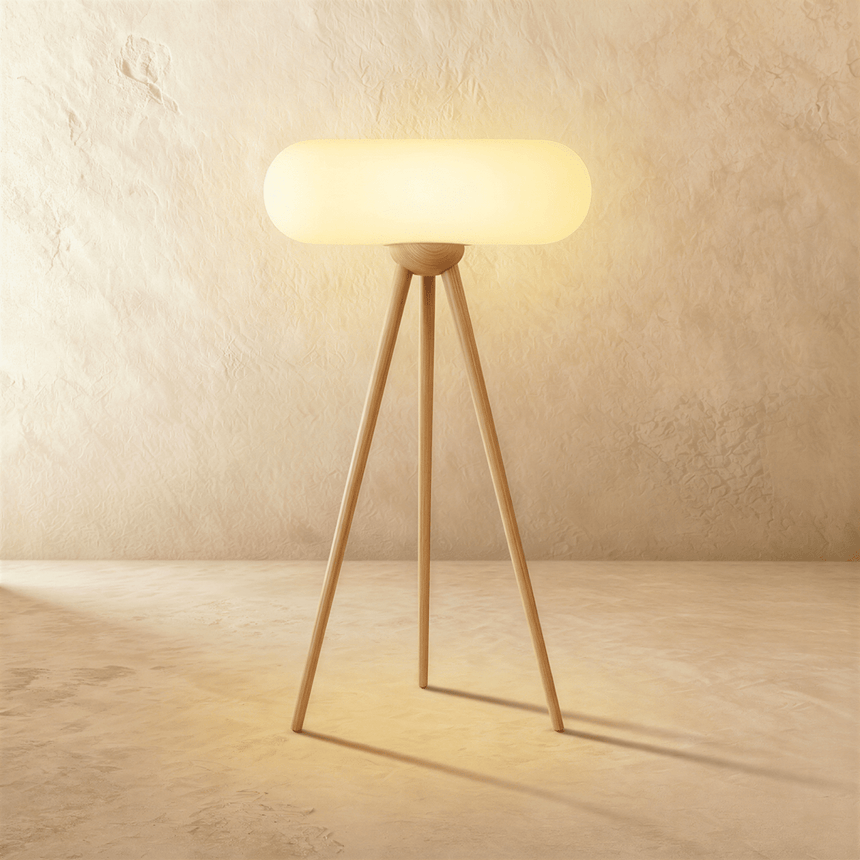 The same tripod in natural wood, the pale capsule shade lit above three legs