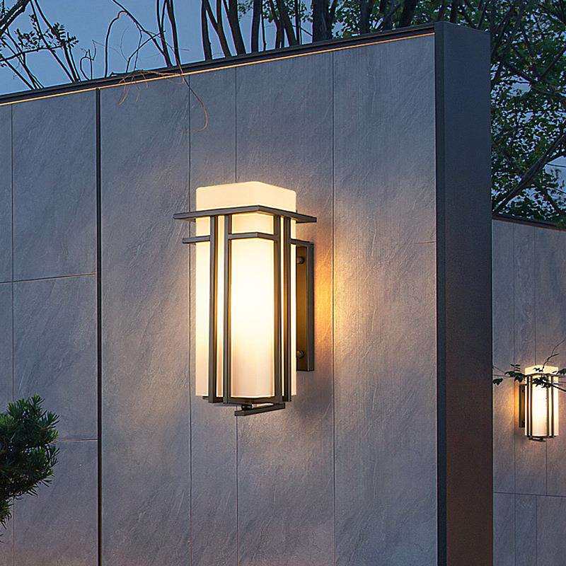 The lantern lit on a gray stone panel wall at dusk, a second one further along