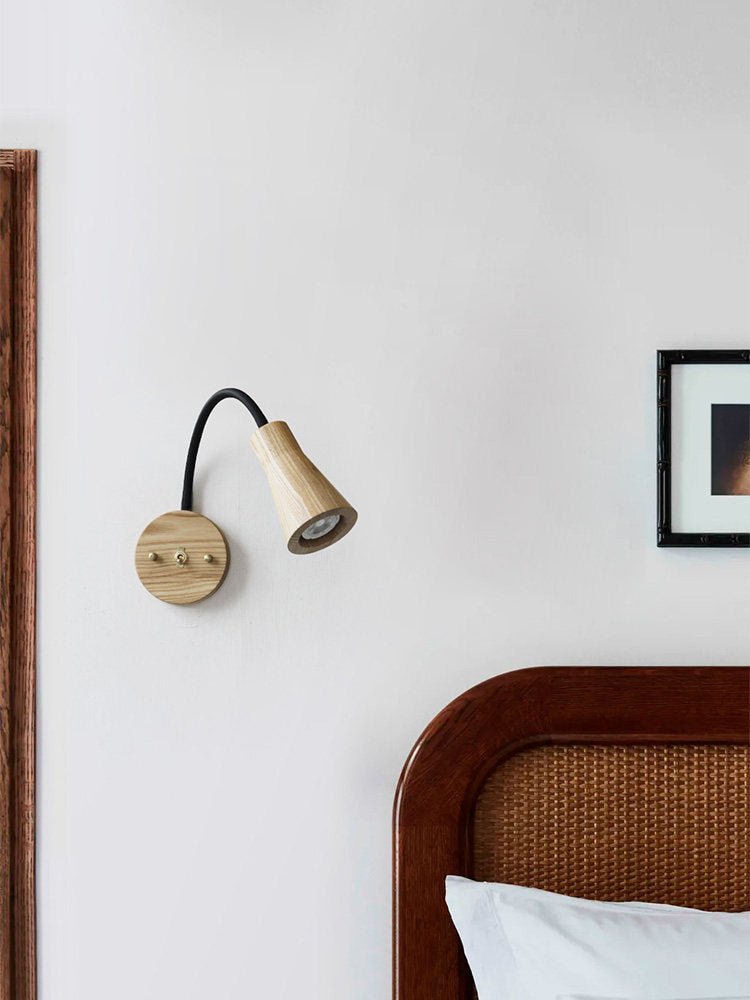 Sconce lit on a white wall beside a cane headboard and a framed print