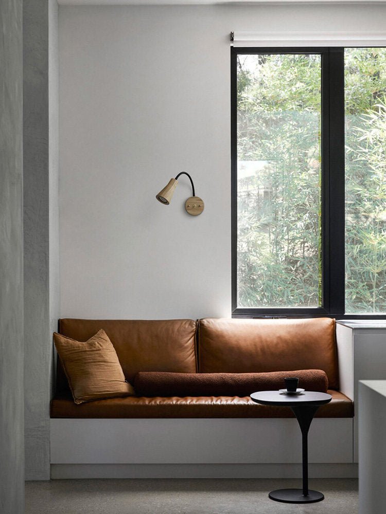 Sconce on a wall above a window bench with a leather seat and cushion