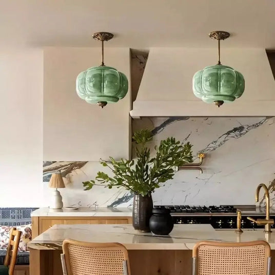 Two green ribbed shades above a marble kitchen island with a vase of leaves