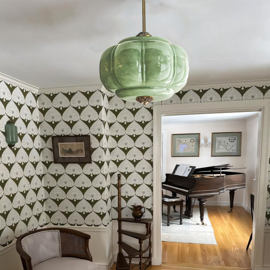 Green ribbed shade lit in a room with patterned wallpaper and a piano beyond