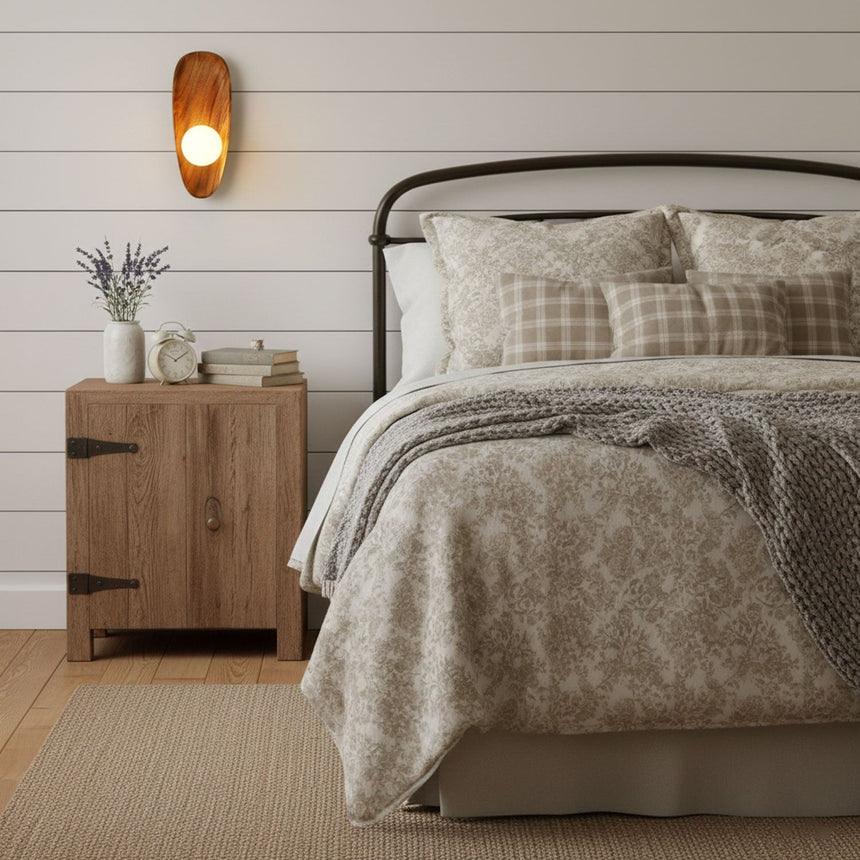 Sconce lit on a plank bedroom wall above a wood dresser beside a bed