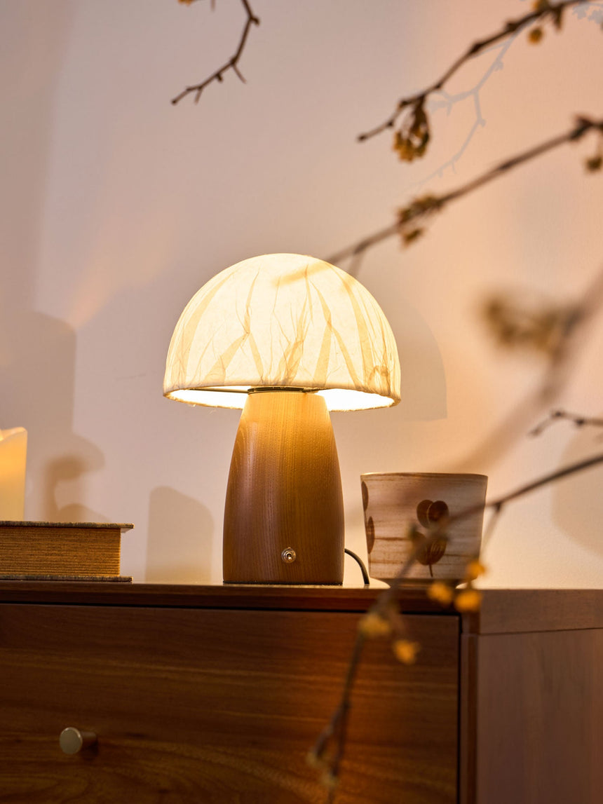 Mini table lamp lit on a chest beside a blossom branch and a candle