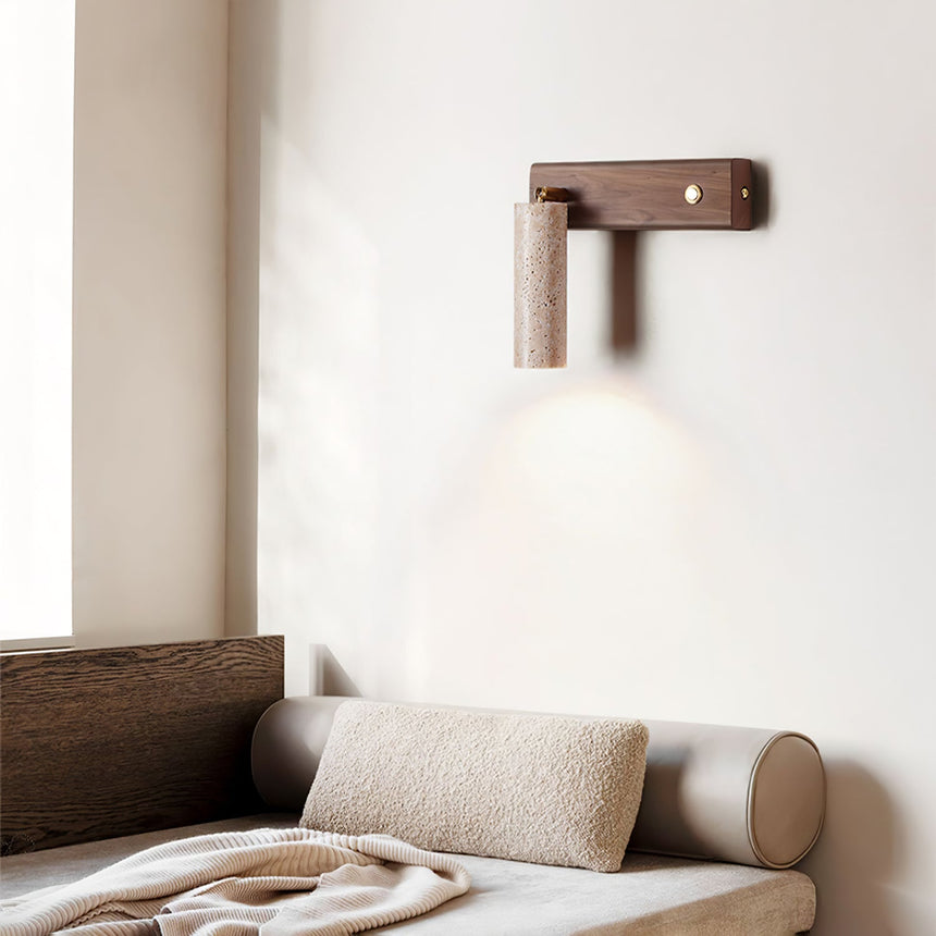 Sconce lit above a bed with a bolster cushion and a folded knit throw