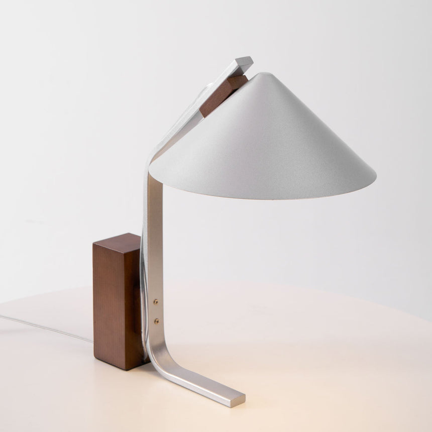 Minimalist desk lamp seen at an angle against a plain pale ground
