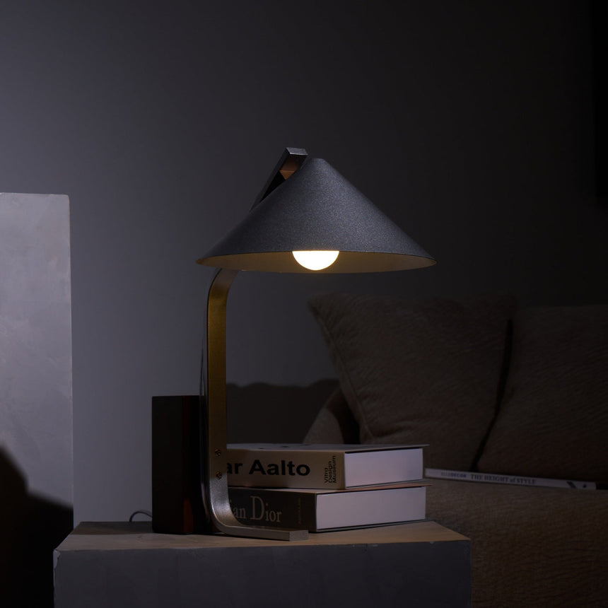 Minimalist desk lamp lit in a dark interior beside books