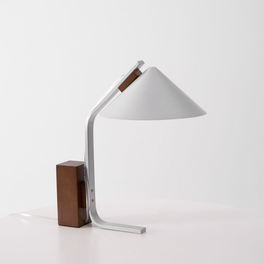 Minimalist desk lamp seen three quarters on against a pale ground