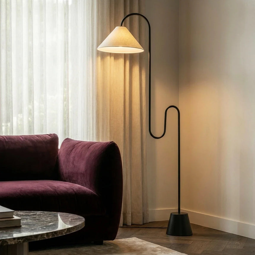 The lit cone shade above a burgundy sofa beside curtains and a round table