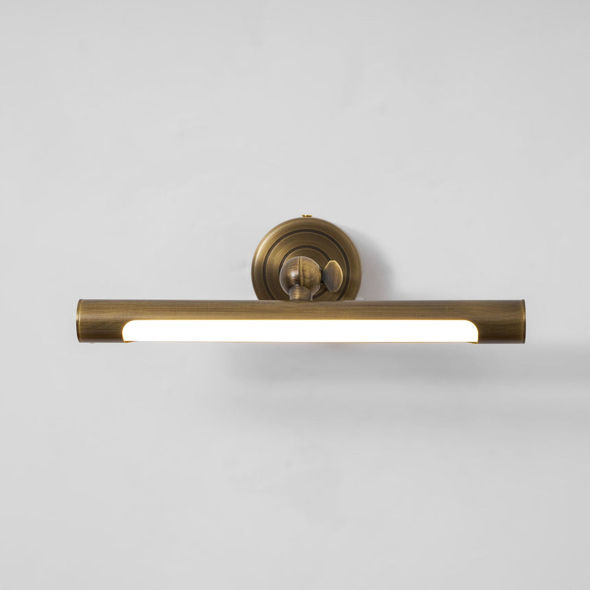 The bronze bar lit along its length, the diffuser bright below the round plate