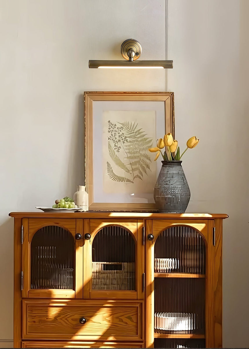 Bronze bar lit over a framed print standing on a cane fronted wood cabinet
