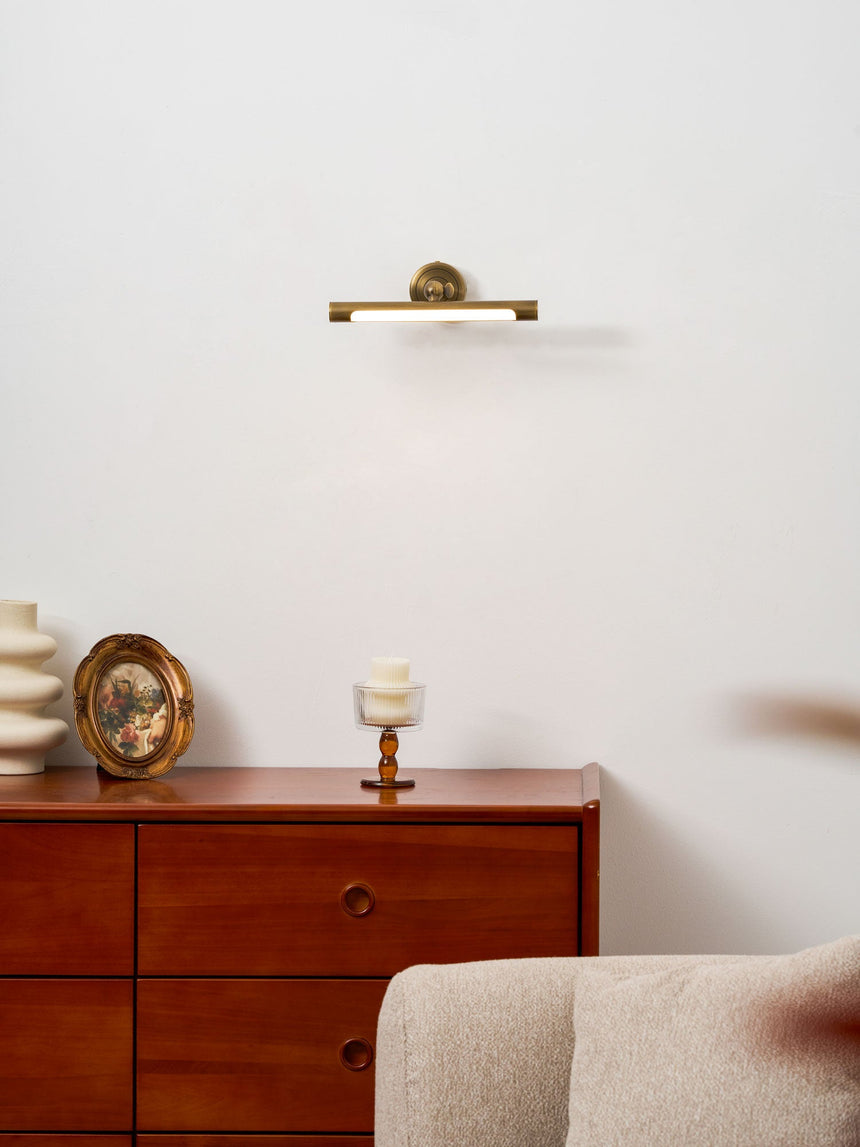 Bronze bar lit above a red wood dresser with a small round mirror and candles