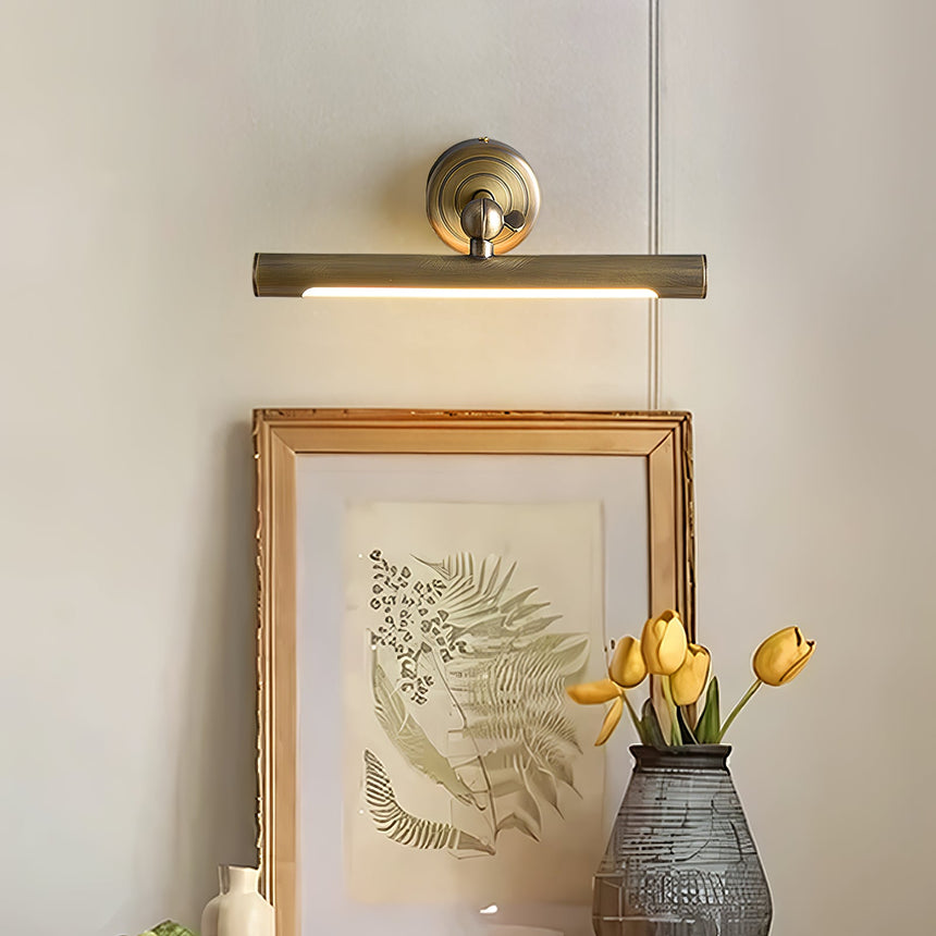 Bronze bar lit above a gilt framed fern print beside a vase of yellow tulips