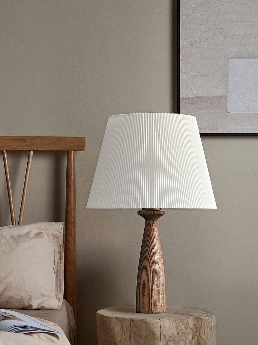 Ribbed shade lamp unlit on a wood stump table beside a made bed