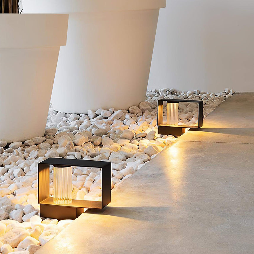 Two low bodies lit in a white pebble bed beside a pale terrace