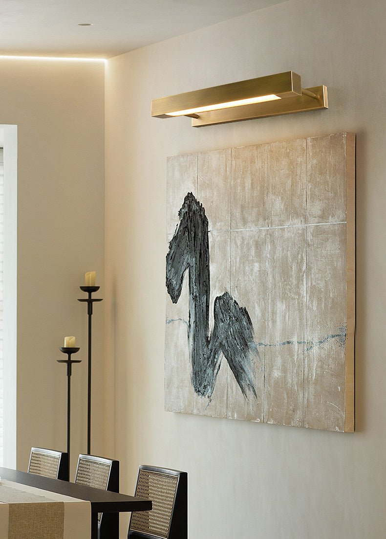 Brass bar lit over a framed artwork on a wall beside dining chairs
