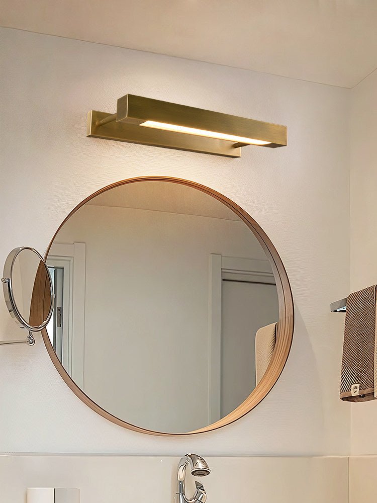 Brass bar lit above a round mirror on a bathroom wall beside a towel rail