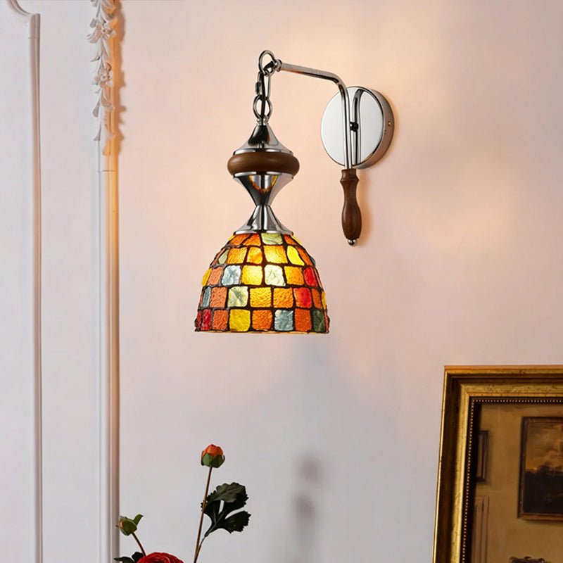 The mosaic shade lit on a pink wall beside white molding and a gilt frame