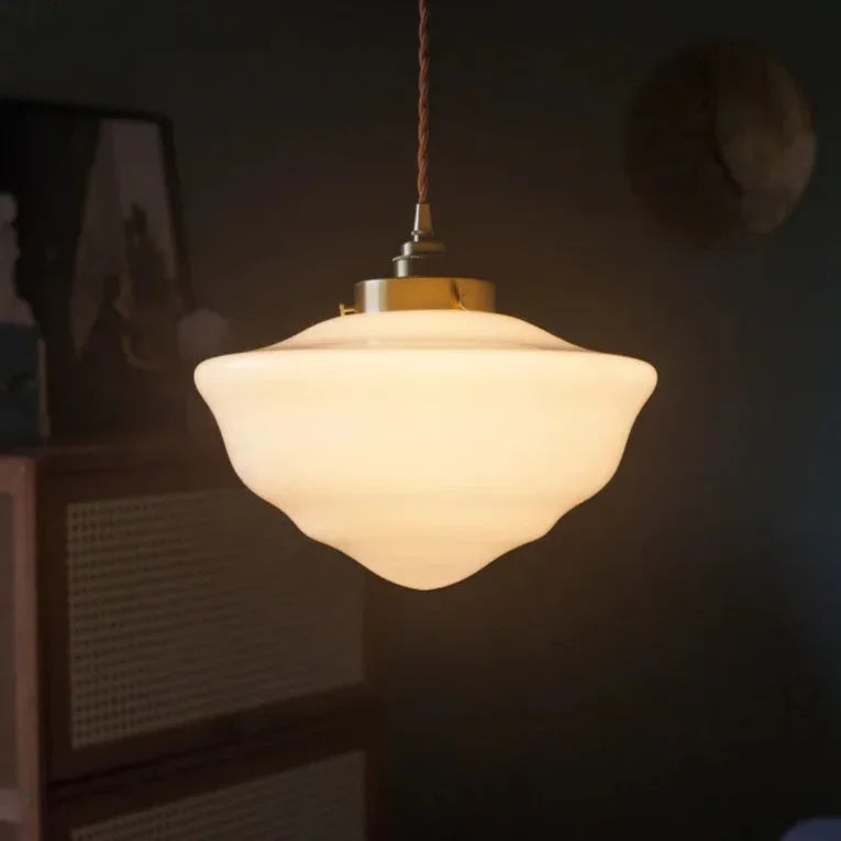 The opal shade lit above a wall of framed artwork in a dim room