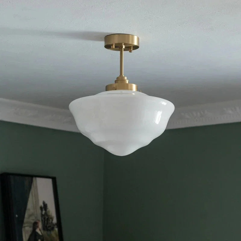 A single opal schoolhouse shade on a brass fitting against a dark green wall